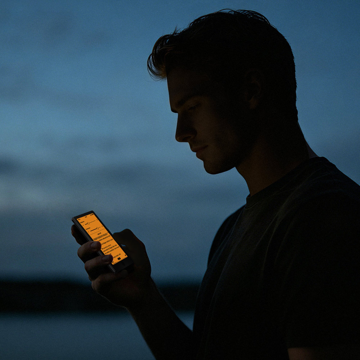 Black pocket eReader held outdoors at night, screen glowing orange