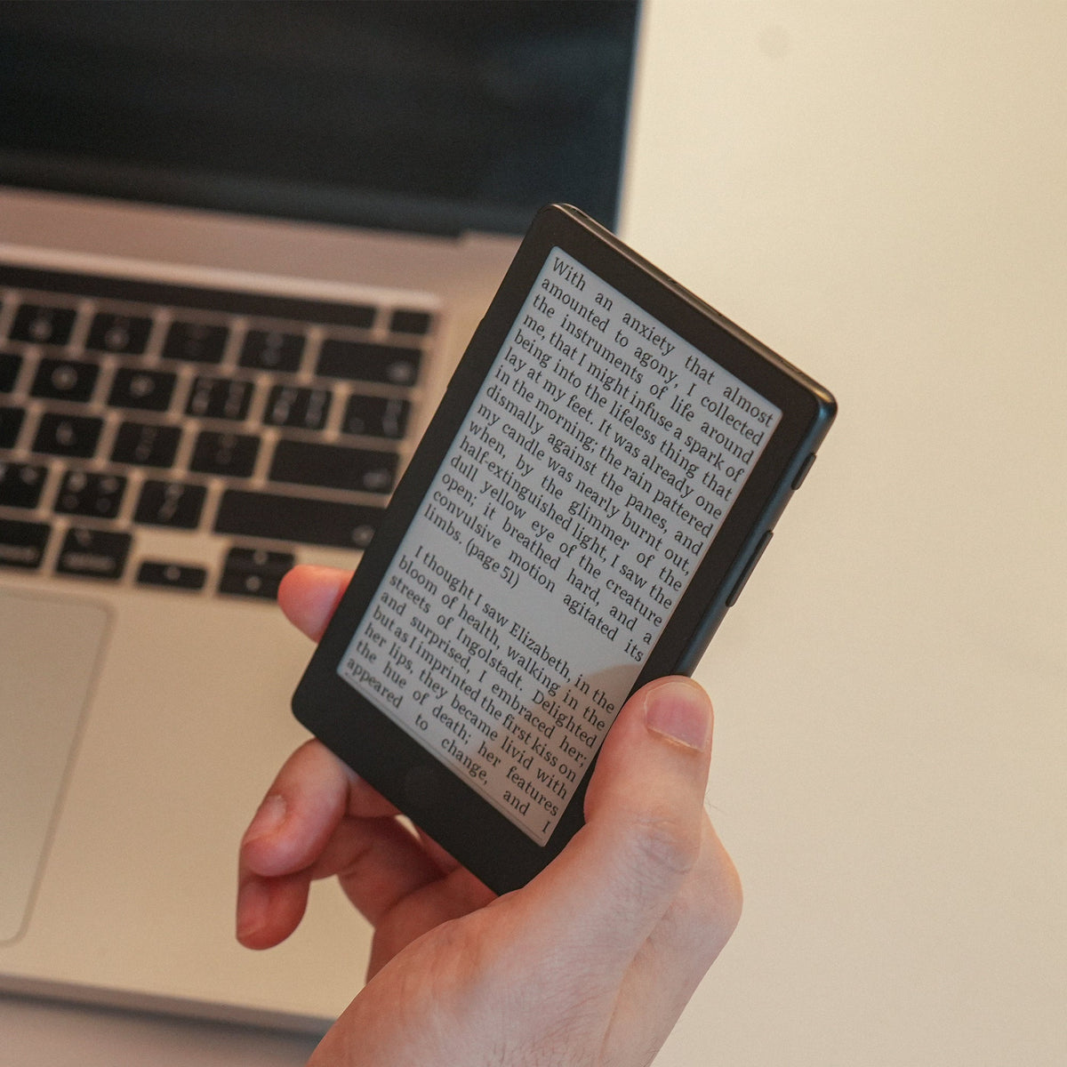 Pocket eReader showing dense text on a dark screen while held over a laptop